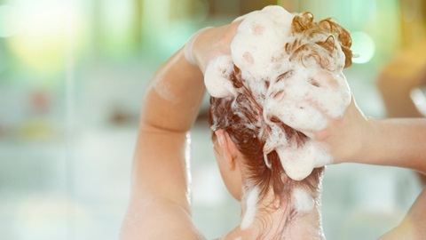 Une dame, vue de dos, se lave les cheveux avec du shampoing.
